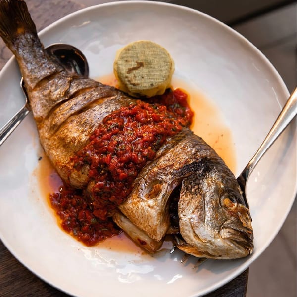Whole roasted fish topped with red sauce and a round green garnish on a white plate.