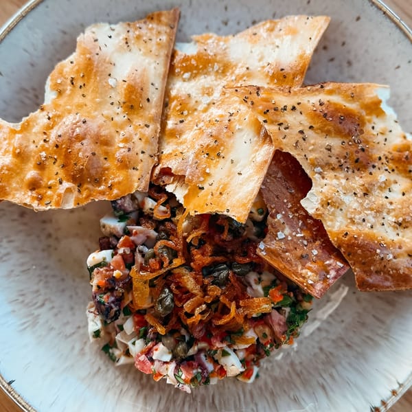 Broma Restaurant's American dish with crispy flatbread, chopped salad, and fried onions.