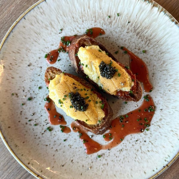 Two pieces of uni toast with caviar and chives on a white plate with red sauce.